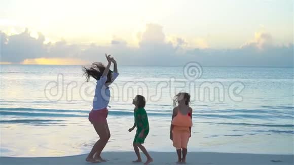 可爱的小女孩和年轻的母亲在热带海滩在温暖的晚上跳舞和乐趣日落时分的家人视频的预览图