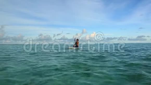 坐在冲浪板上的年轻人印度洋平静的海水令人惊叹的美丽绿松石水和蓝天白云视频的预览图