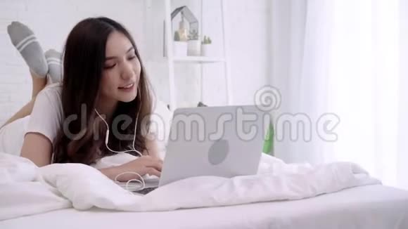 快乐的女性用耳机听音乐在家里用笔记本电脑搜索歌曲生活方式女性在家里的概念视频的预览图