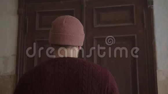 穿着针织毛衣和帽子的人站在紧闭的棕色门前打开它们视频的预览图