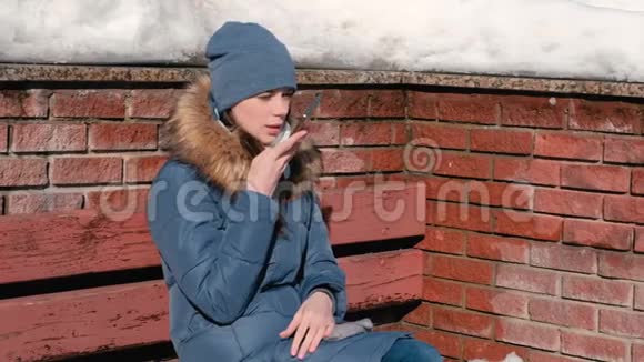 女人坐在冬季公园的手机上讲音频信息视频的预览图