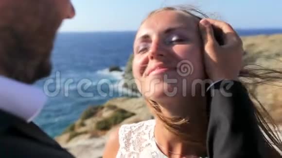 一位快乐的新郎在阳光明媚的风日在海滩上亲吻新娘特写视频的预览图