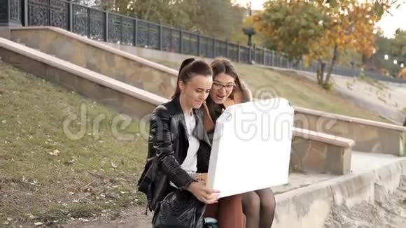 两个女孩坐在公园里吃着美味的大披萨里面有鸡肉和蘑菇视频的预览图
