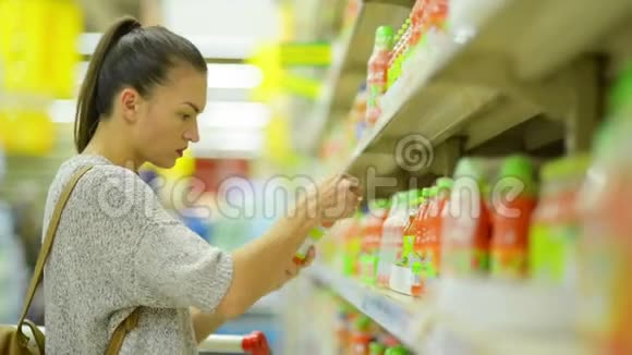 在货架附近的超市里挑选果汁的漂亮少女特写镜头视频的预览图