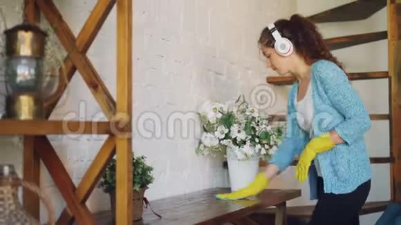 有魅力的家庭主妇正在打扫家具通过无线耳机听收音机跳舞女孩视频的预览图