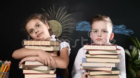 学校观念可爱的男孩和迷人的女孩坐着一堆书学童坐在书桌旁后面的黑板视频的预览图