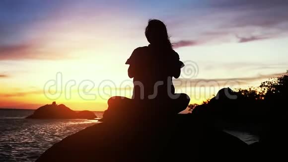 美丽的风景女人做瑜伽冥想在海边的岩石上日落背景慢动作1920x1080视频的预览图