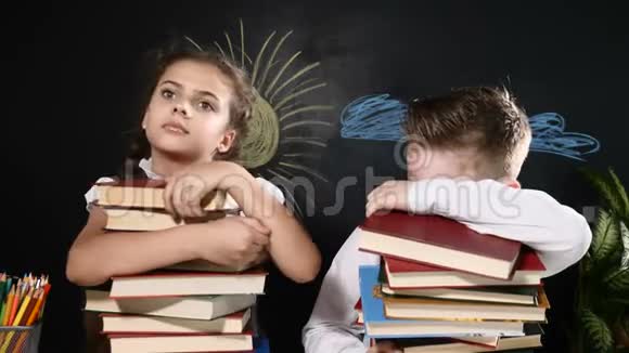 学校观念可爱的男孩和迷人的女孩坐着一堆书学童坐在书桌旁后面的黑板视频的预览图