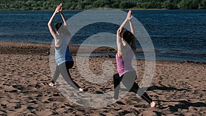 两个女人在城市河边的沙滩上做瑜伽日出时美丽的城市景色特里科纳桑乌蒂哈的姿势视频的预览图