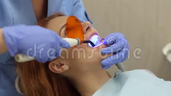 牙医的女孩牙医医生用紫外线灯照在她的牙齿上视频的预览图
