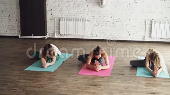 年轻灵活的妇女正在做各种伸展运动坐在瑜伽垫在漂亮的灯光工作室它们在弯曲视频的预览图