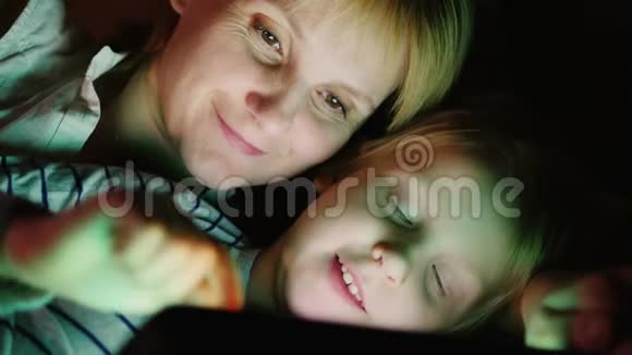 快乐的母亲和她的女儿我一起玩平板电脑面对面躺在床上视频的预览图