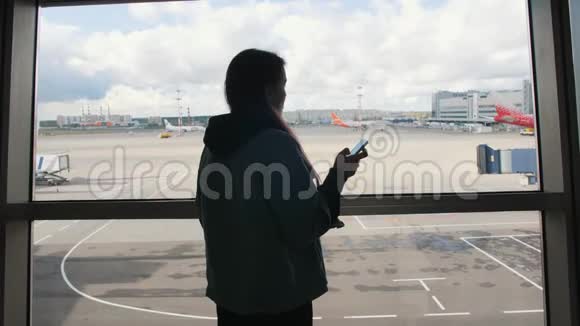 青年混合种族旅游妇女使用移动电话靠近窗口在出发机场航站楼4K视频的预览图