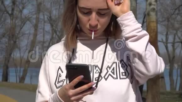 女孩带着棒棒糖与朋友传递信息站在公园与滑板视频的预览图