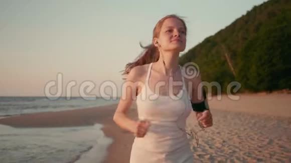苗条的女跑步者是在日落或海上日出的海滩上慢跑视频的预览图
