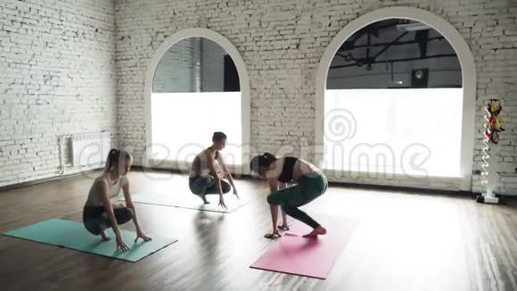 年轻女性练习瑜伽的多莉镜头在灯光工作室的木地板上在明亮的垫子上做前屈姿势视频的预览图