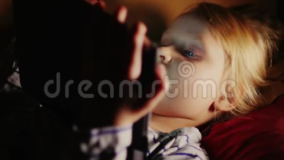 女孩躺在床上用平板电脑一个发光的平板屏幕在黑暗中照亮了女孩脸视频的预览图