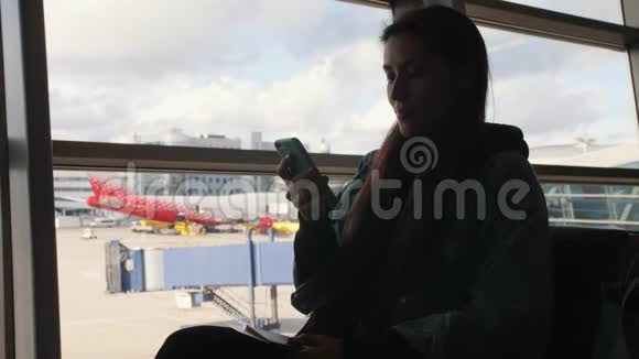 青年混合种族旅游妇女使用移动电话靠近窗口在出发机场航站楼4K视频的预览图