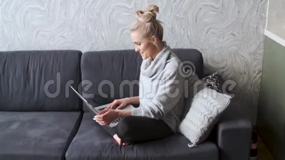 年轻的金发美女坐在客厅的沙发上用笔记本电脑视频的预览图