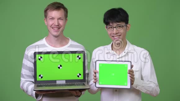 两个快乐的年轻多民族商人向摄像机展示笔记本电脑和数码平板电脑视频的预览图