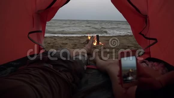 年轻夫妇躺在红色帐篷里关闭男性和女性腿的镜头女孩在给他们打电话视频的预览图