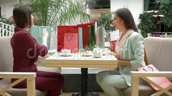 购物日兴高采烈的女人在餐馆里喝茶夸耀自己购买的季节性商品和折扣视频的预览图