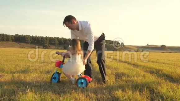 快乐的父亲教小女儿骑自行车爸爸在草坪上和小孩玩孩子学骑自行车视频的预览图