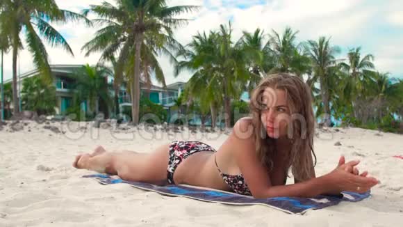 在豪华别墅背景下日光浴的女人躺在夏日海滩上的毛巾上迷人的女人在沙滩上晒黑视频的预览图