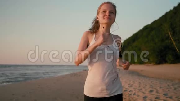 年轻的苗条女跑步者正在海上日落的海滩上慢跑视频的预览图