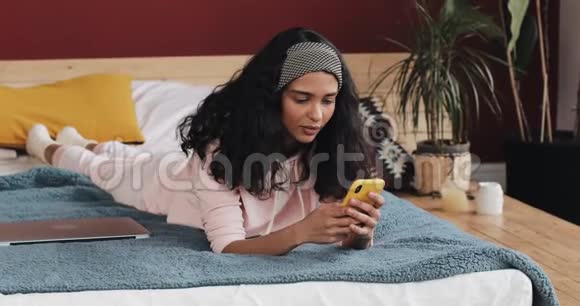 快乐的非裔美国女孩聊天和短信智能手机躺在床上在家里年轻女子视频的预览图