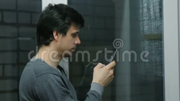 男人正站在阳台的窗户附近用手机浏览网页侧视视频的预览图