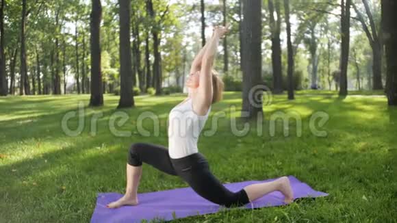 美丽微笑的中年妇女在公园里做瑜伽练习和伸展运动的4K慢动作视频它是非常视频的预览图