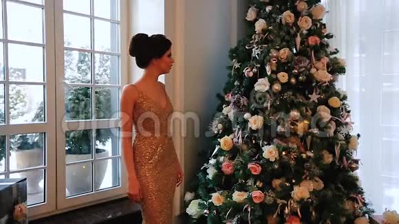 一个穿着晚礼服的漂亮女孩在装饰着圣诞树的房间里做梦视频的预览图