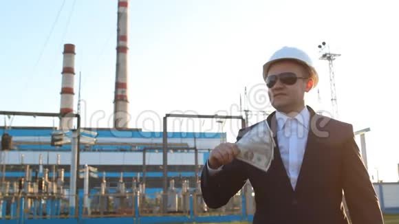 一位年轻而满意的戴着黑眼镜的工程师检查员在发电厂背景下拿着钱视频的预览图