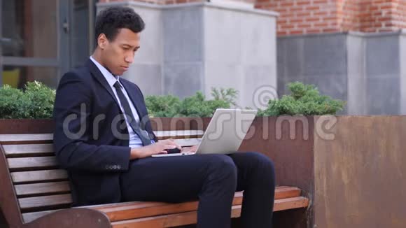 损失非洲商人坐在板凳上对笔记本电脑的成绩感到沮丧视频的预览图