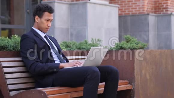 兴奋的非洲商人在坐在长凳上的笔记本电脑上庆祝成功视频的预览图
