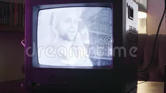 穿着毛衣和袜子帽的长胡子的成熟男人正在被旧电视所播放视频的预览图