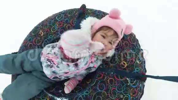 冬天休闲和娱乐的概念快乐的小女孩躺在雪橇上在运动中挥手视频的预览图