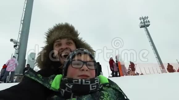 一个年轻人带着一个快乐的男孩在冬天在冰上坐过山车英俊的爸爸和儿子在笑视频的预览图
