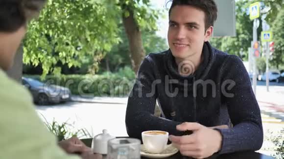 年轻人坐在咖啡馆的露台上和朋友聊天视频的预览图