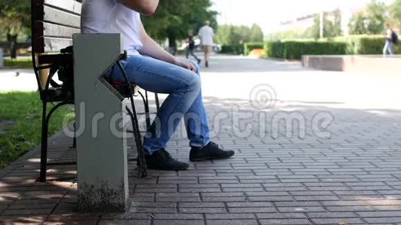 市中心的一个人坐在长凳上把水抽干把一个塑料瓶子扔过垃圾桶扔垃圾视频的预览图