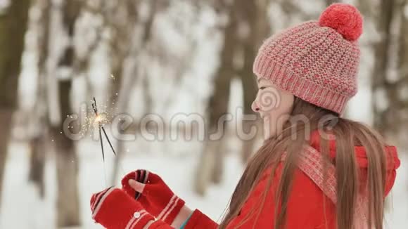一个快乐的年轻女学生在冬天的森林里闪耀着孟加拉灯的火花在新年前夕视频的预览图