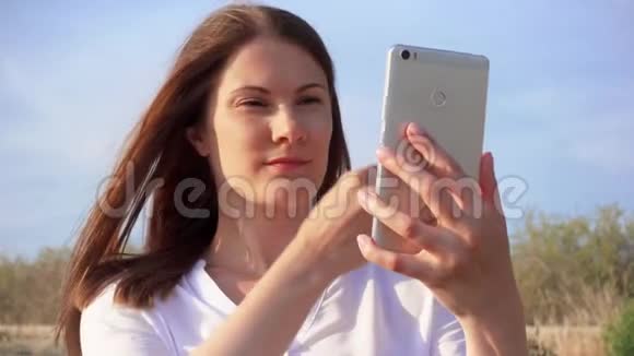 女人用手机对抗蓝天微笑女性慢动作在手机上自拍视频的预览图