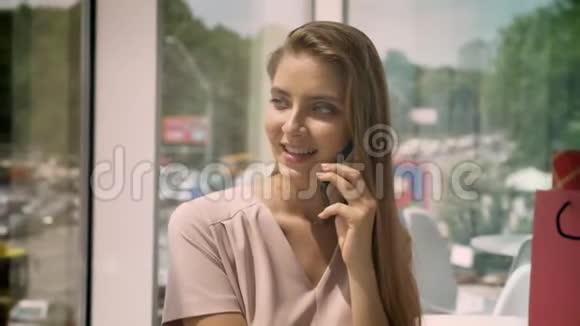 年轻漂亮的女孩白天坐在有大窗户的咖啡馆里在智能手机上聊天交流的概念视频的预览图