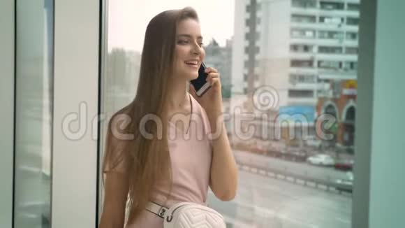 年轻漂亮的女孩坐在窗户上白天在智能手机上聊天交流概念城市概念视频的预览图