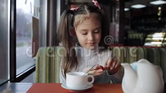 漂亮的小女孩正在咖啡馆里吃午饭女婴吃糖果和调味茶视频的预览图