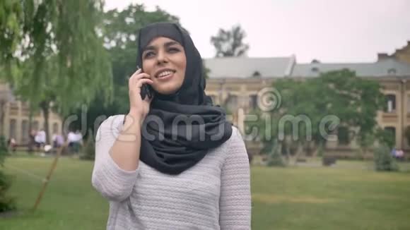 戴头巾的年轻穆斯林女孩正在公园的蓝色天气里打电话在背景的基础上建立了宗教观念视频的预览图