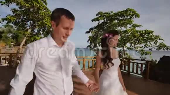 新娘和新郎携手走在酒店的露台上俯瞰大海从视频的预览图