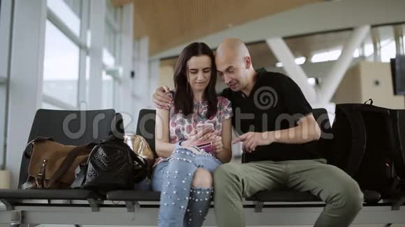 在机场候机大厅穿着休闲服的男孩和女孩看着坐在黑色椅子上的写字板视频的预览图