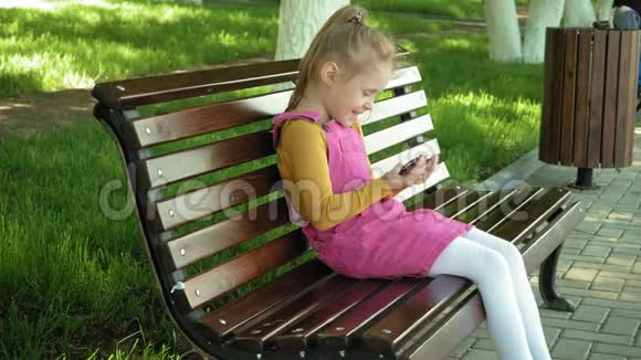 一个学龄前的微笑女孩在公园户外使用电话夏日阳光明媚视频的预览图